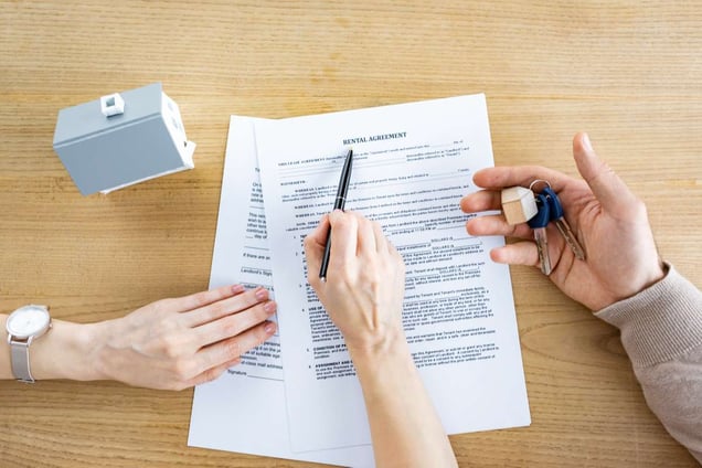 Top view of woman holding pen near document with rental agreement lettering and man with keys in hand (R) (S)