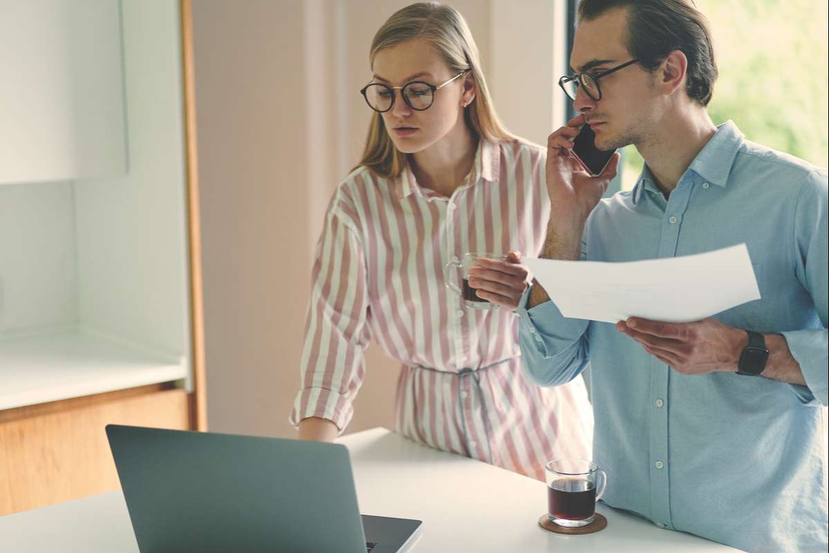 Young couple standing on the modern kitchen with laptop and smartphone while working from home (R) (S)